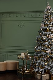 Beautiful Christmas tree, gift boxes, table and festive decor near olive wall indoors. Interior design