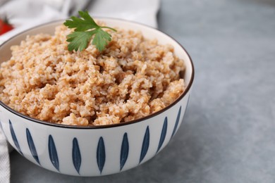 Tasty wheat porridge with parsley in bowl on grey table, closeup. Space for text