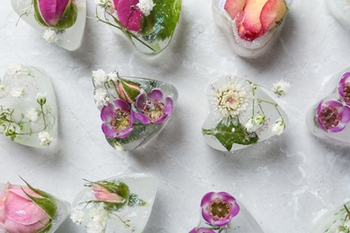 Photo of Heart shaped ice cubes with flowers on grey background, flat lay