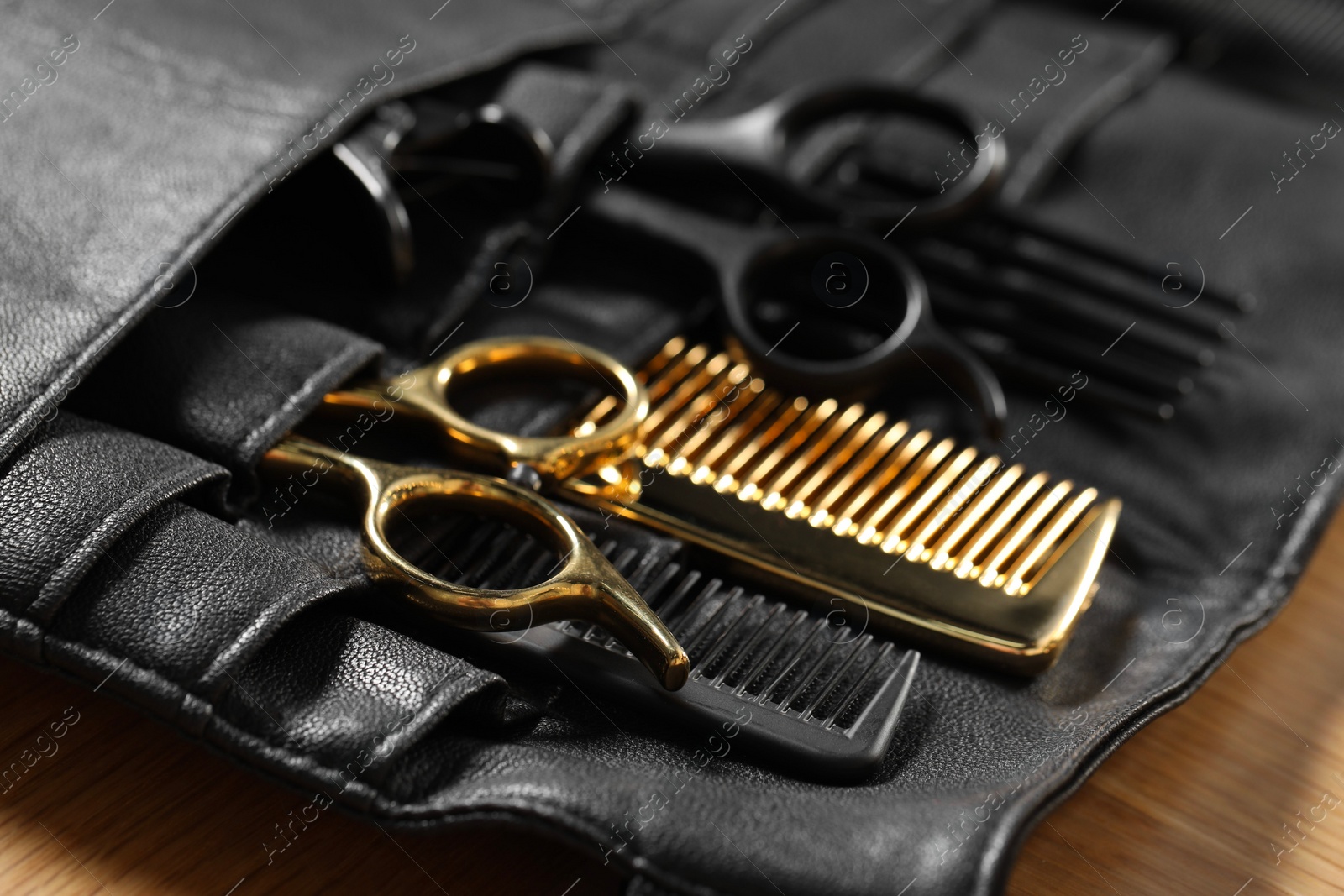 Photo of Hairdresser tools. Professional scissors and combs in leather organizer on wooden table, closeup