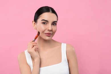 Photo of Beautiful woman applying makeup with brush on pink background, space for text