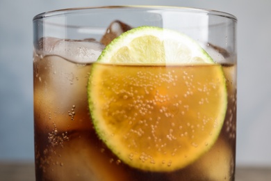 Glass of refreshing soda drink with ice cubes and lime on blue background, closeup