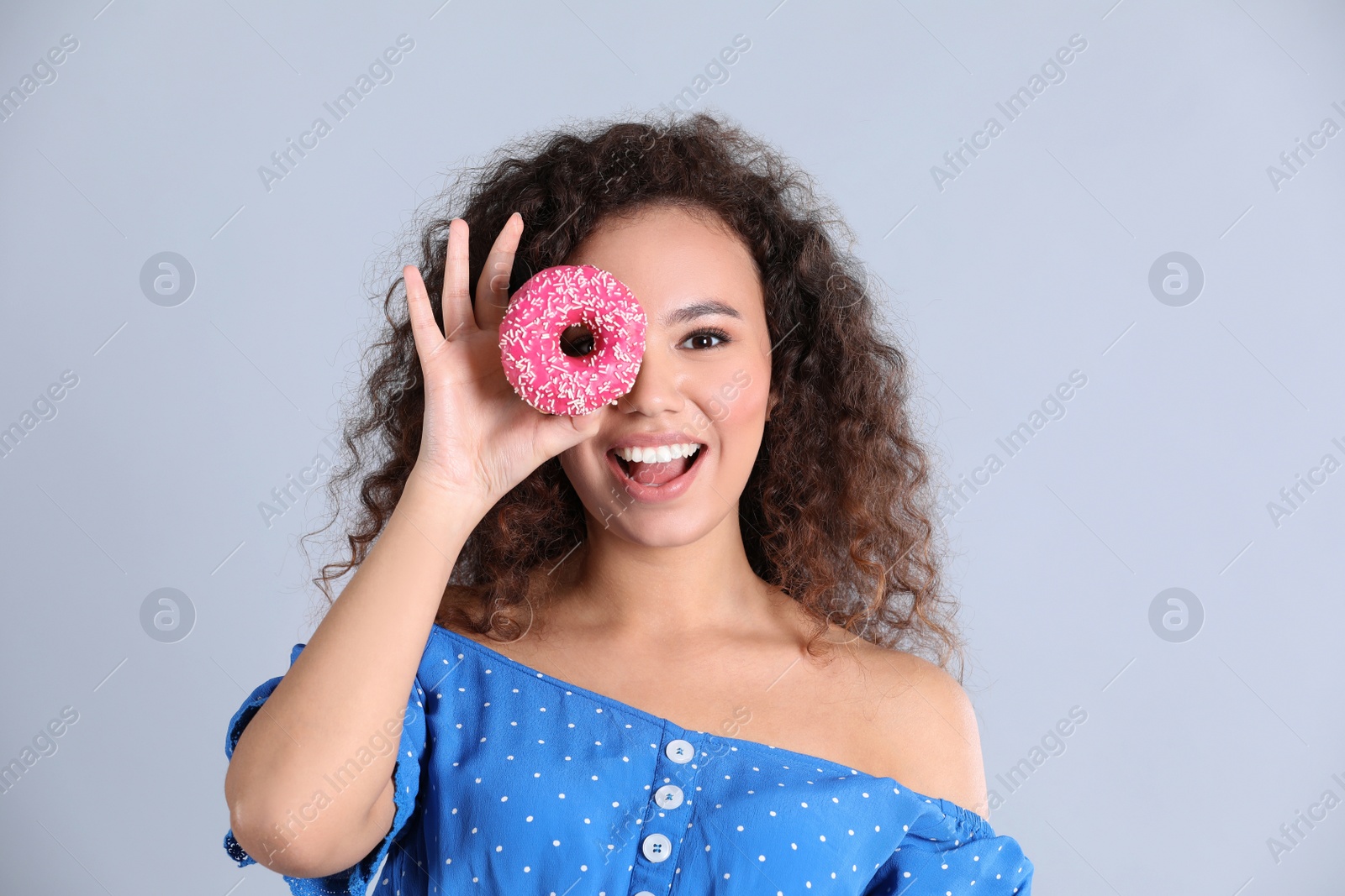 Photo of Beautiful African-American woman with donut on light grey background
