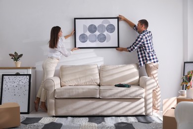 Photo of Happy couple hanging picture on white wall together. Interior design