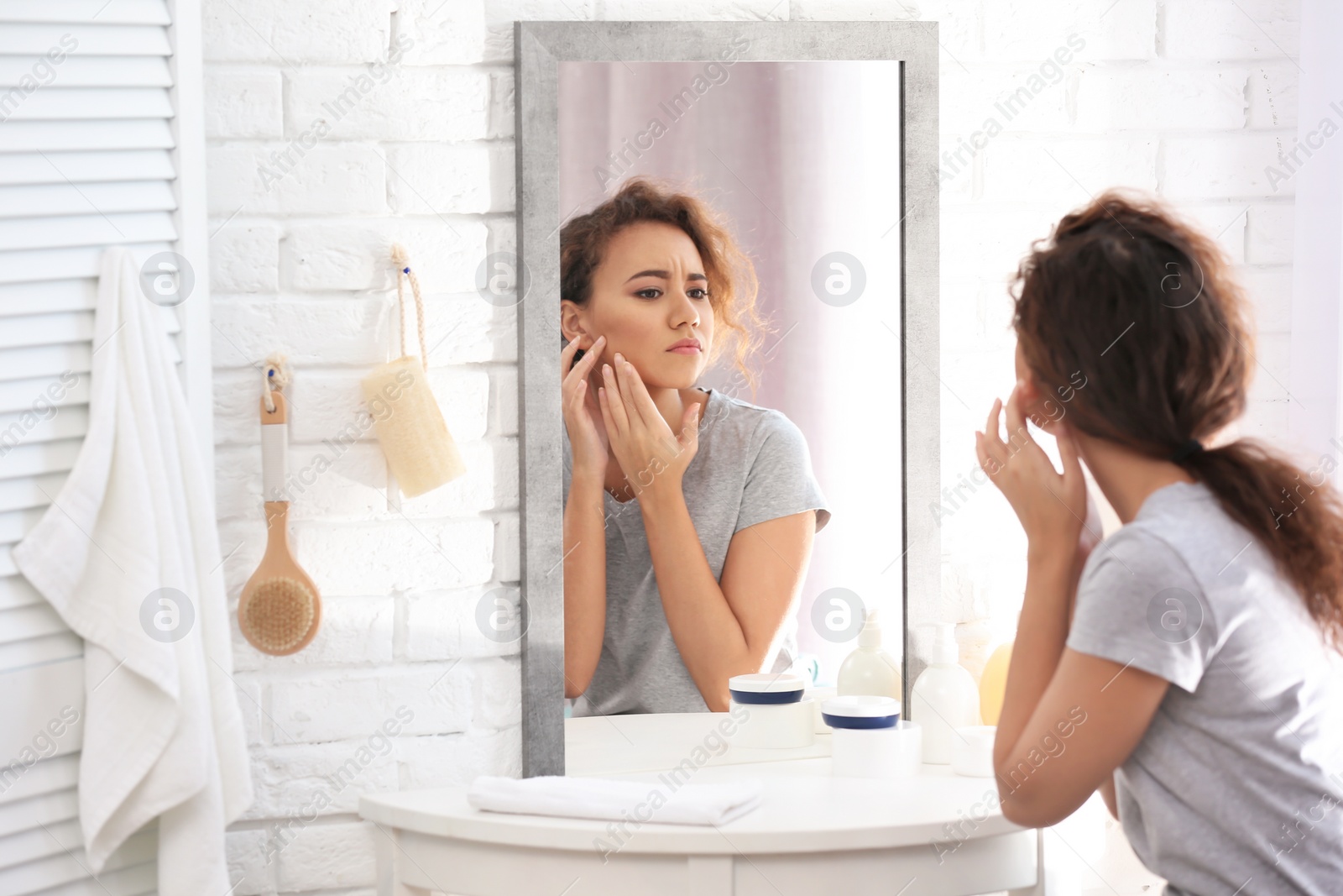 Photo of Beautiful young woman with acne problem looking in mirror at home