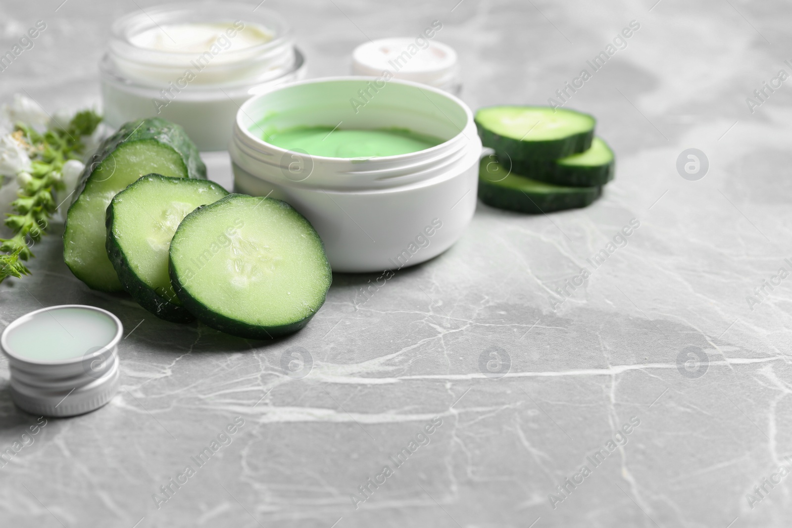 Photo of Jars of body cream and cucumber slices on grey marble background. Space for text