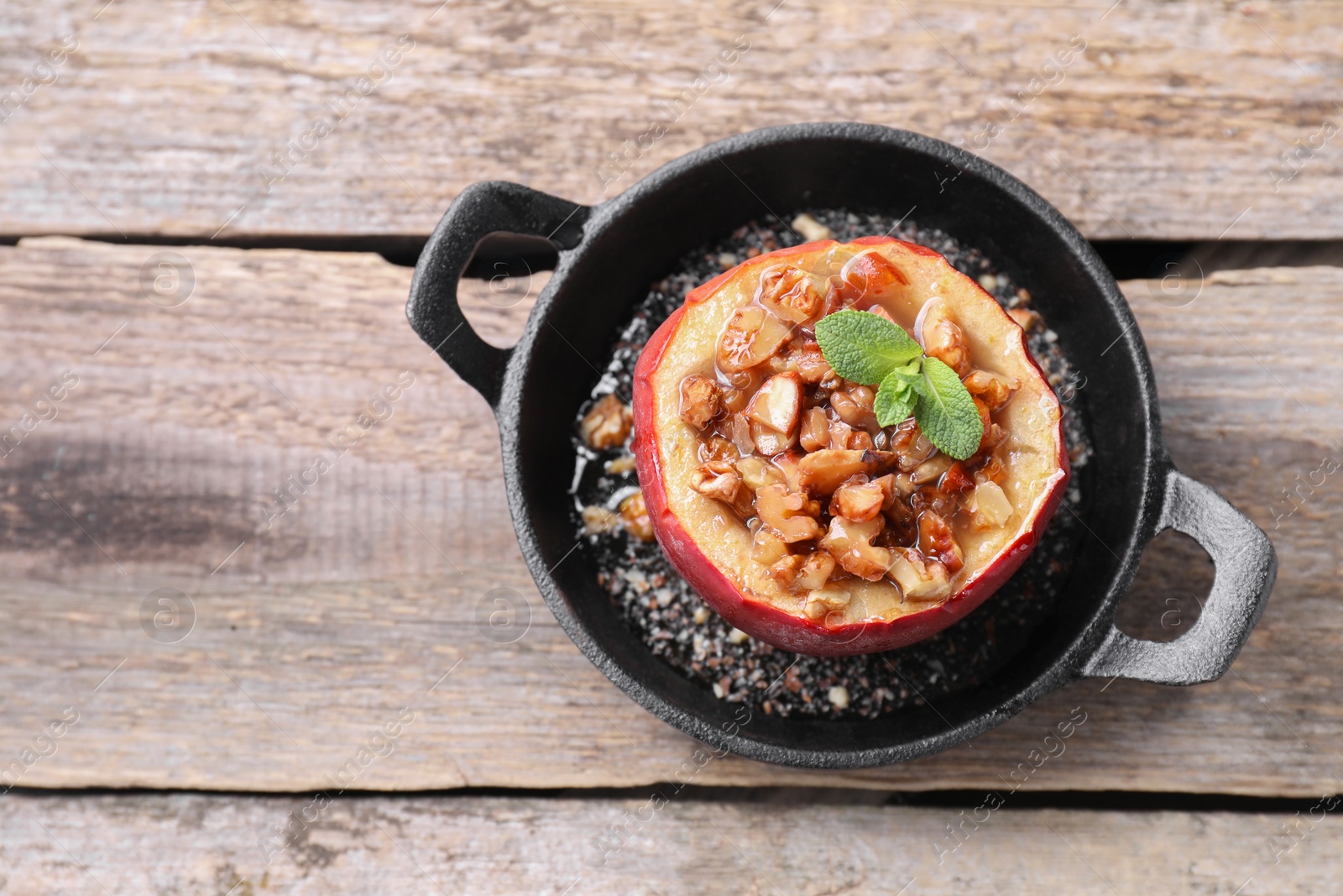 Photo of Tasty baked apple with nuts, honey and mint in baking dish on wooden table, top view. Space for text