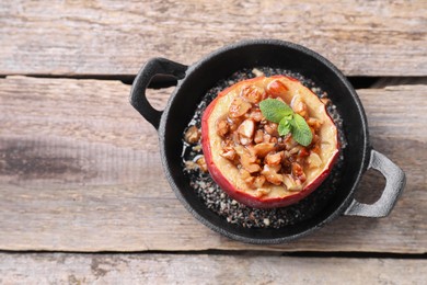 Photo of Tasty baked apple with nuts, honey and mint in baking dish on wooden table, top view. Space for text