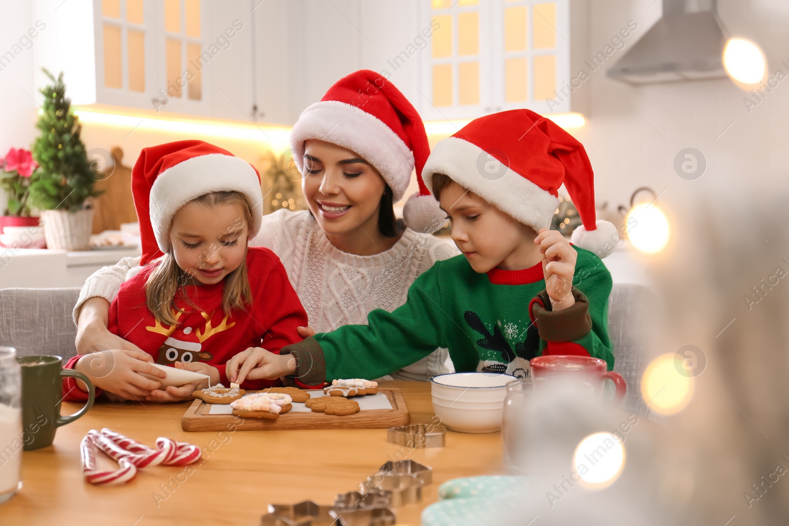 Photo of Mother and her cute little children decorating tasty Christmas cookies at table in kitchen