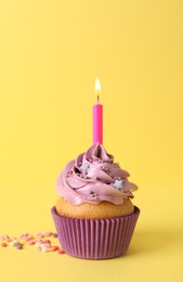 Photo of Birthday cupcake with burning candle and sprinkles on yellow background