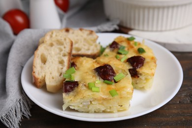 Photo of Tasty sausage casserole with green onion and bread on wooden table, closeup