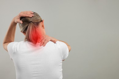 Woman suffering from neck pain on grey background, back view