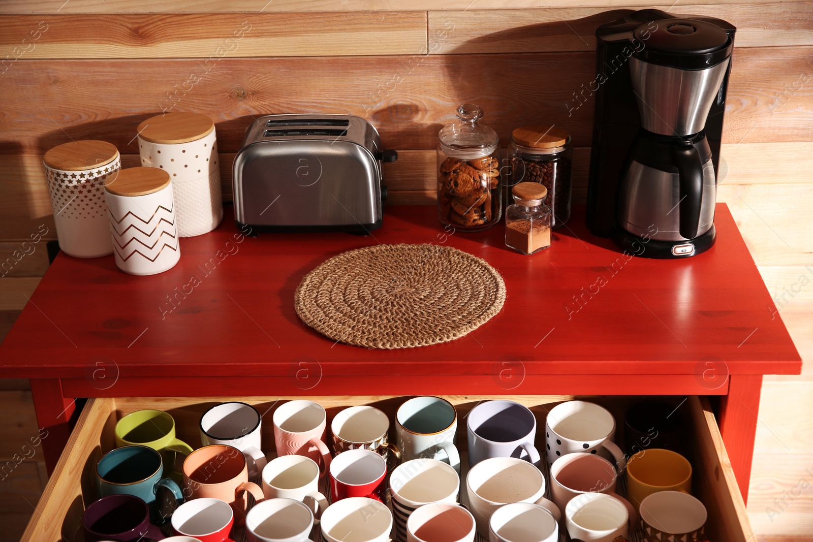 Photo of Open drawer with cups and coffeemaker near wooden wall indoors