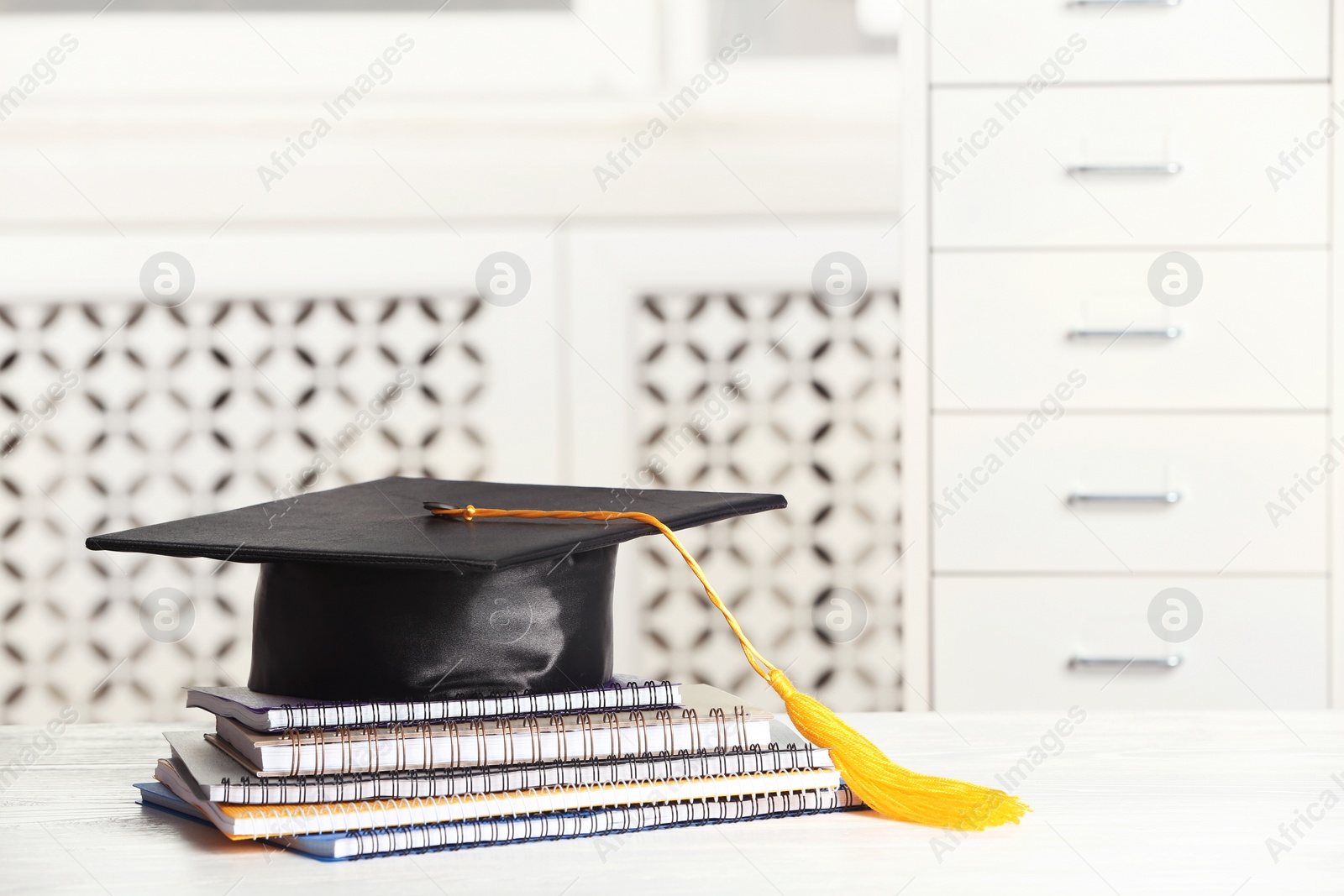 Photo of Graduation hat with notebooks and notebooks on table against blurred background. Space for text