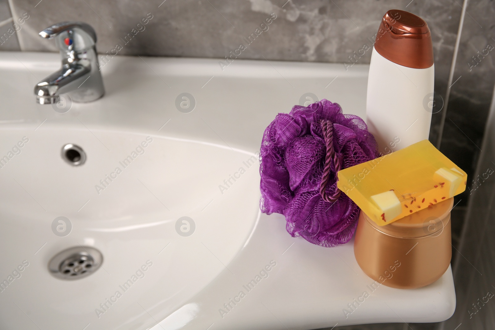 Photo of Purple shower puff and cosmetic products on sink in bathroom, space for text