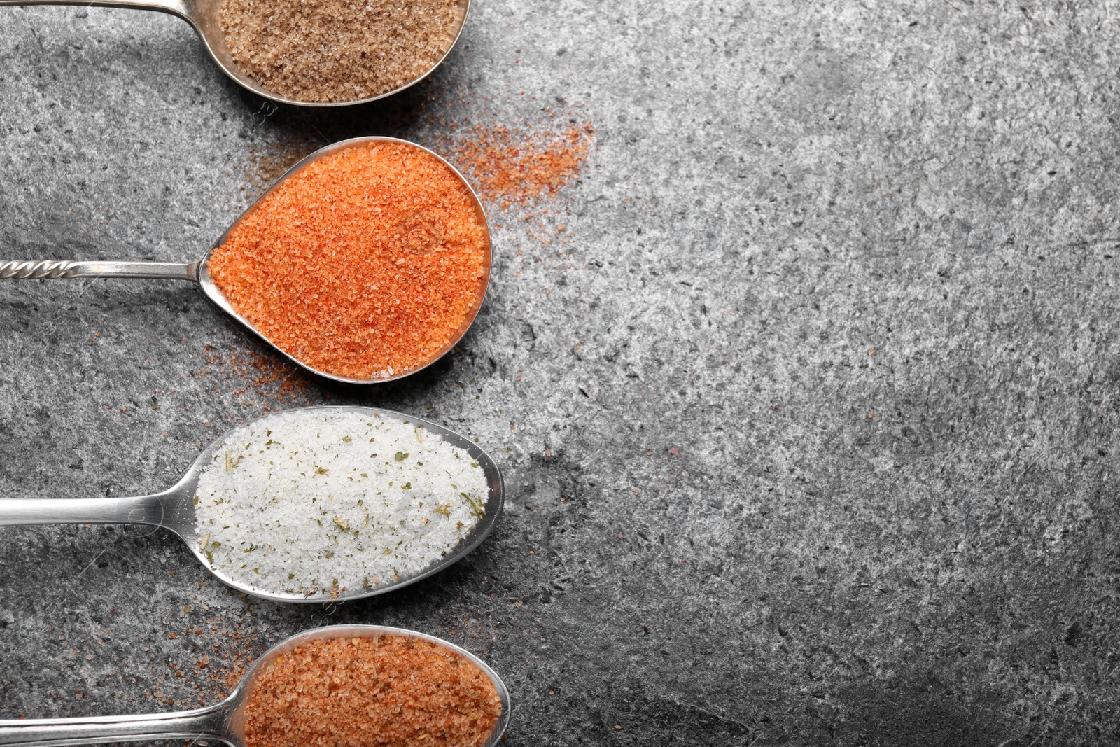 Photo of Different kinds of salt on grey table, flat lay. Space for text