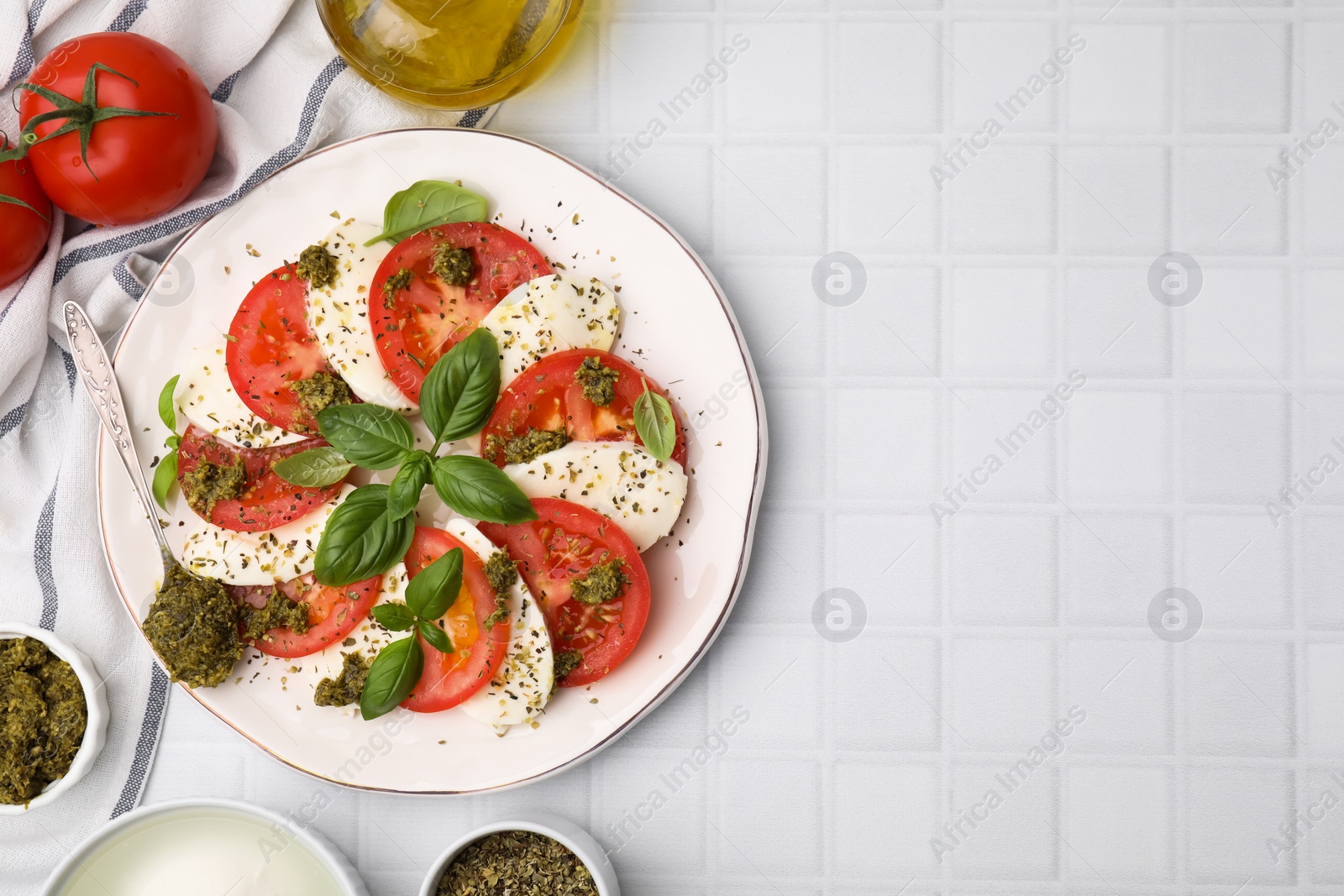 Photo of Plate of delicious Caprese salad with pesto sauce on white tiled table, flat lay. Space for text