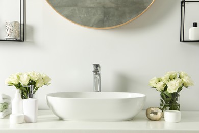 Photo of White sink between beautiful roses and toiletries in bathroom