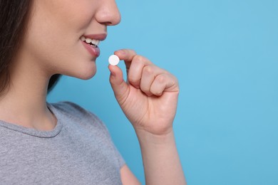 Woman taking pill on light blue background, closeup. Space for text