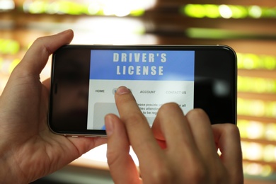 Woman using smartphone to fill driver's license application form against blurred background, closeup