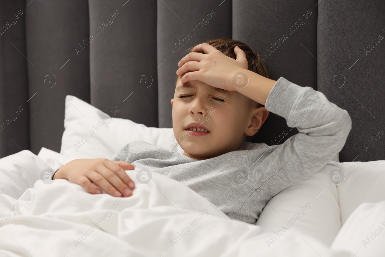 Photo of Little boy suffering from headache in bed at home