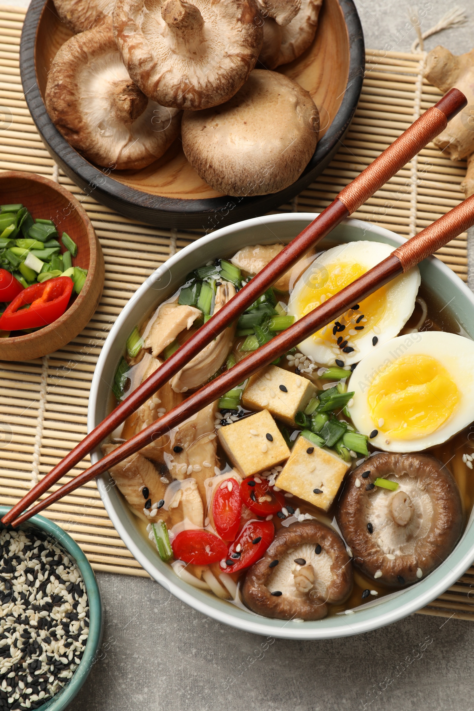 Photo of Bowl of delicious ramen and ingredients on grey table, flat lay. Noodle soup