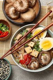 Bowl of delicious ramen and ingredients on grey table, flat lay. Noodle soup