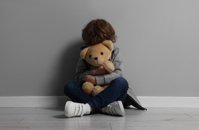 Photo of Child abuse. Upset boy with toy sitting on floor near grey wall