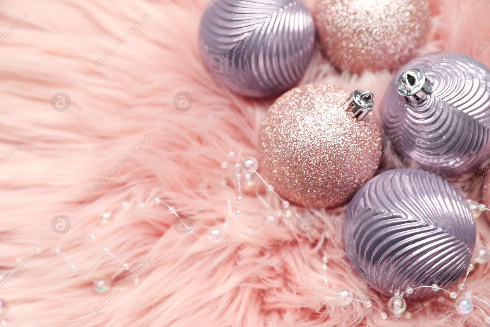 Photo of Beautiful Christmas baubles on pink faux fur. Space for text