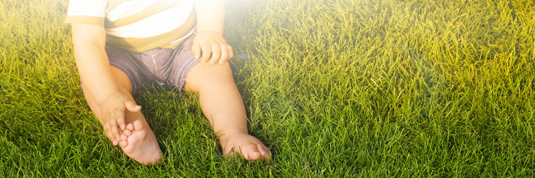 Image of Adorable little baby sitting on green grass outdoors, space for text. Banner design