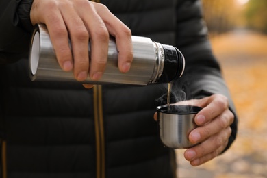 Photo of Man pouring drink from thermos into cap outdoors, closeup