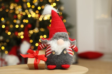 Photo of Funny Christmas gnome and gift box on coffee table in room with festive decoration