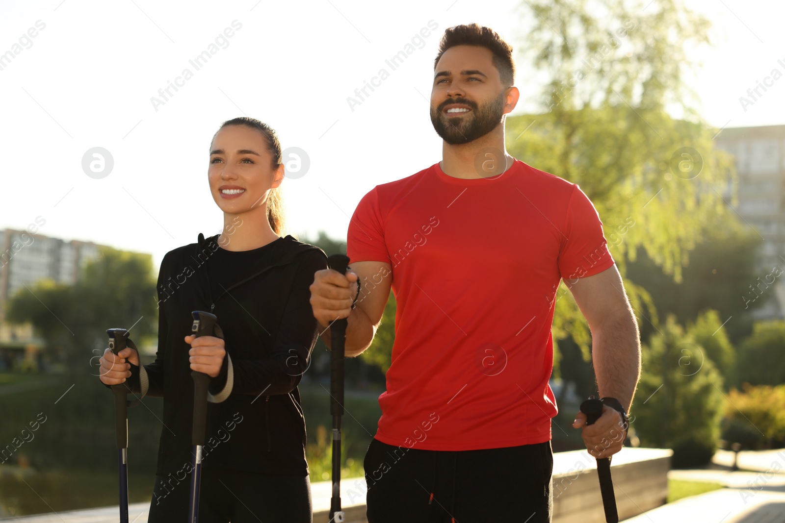 Photo of Happy couple practicing Nordic walking with poles outdoors on sunny day