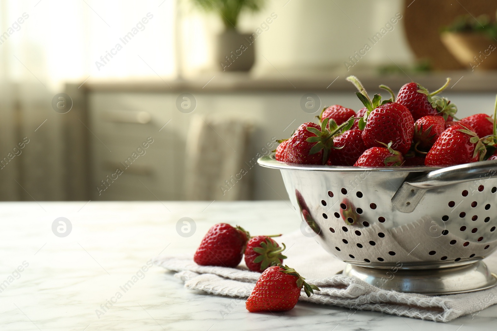 Photo of Metal colander with fresh strawberries on white marble table in kitchen, space for text