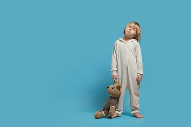 Photo of Boy in pajamas with toy bear sleepwalking on light blue background, space for text