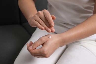 Photo of Woman applying cosmetic cream onto hand on sofa, closeup