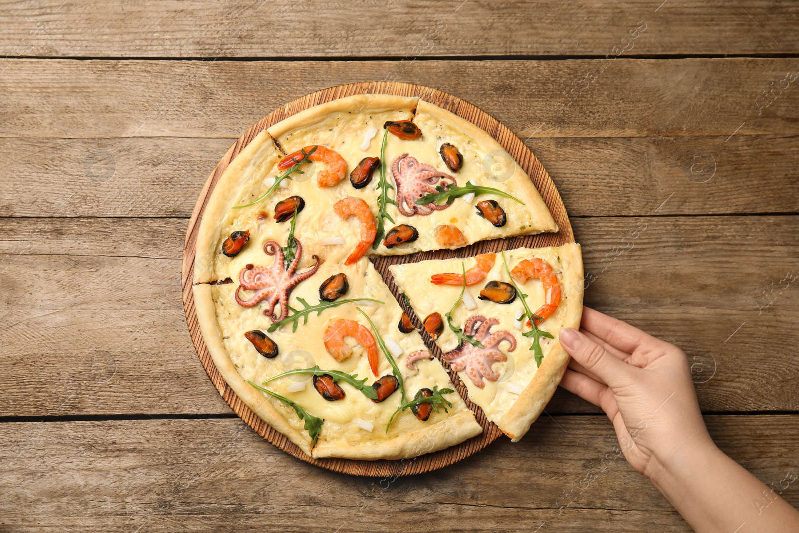 Photo of Woman taking piece of delicious seafood pizza at wooden table, top view