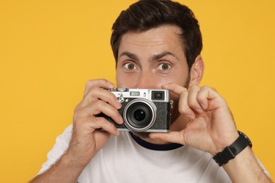 Man with camera taking photo on yellow background. Interesting hobby