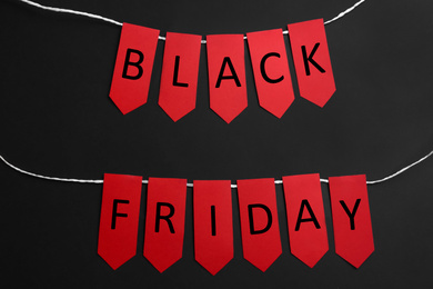 Photo of Words BLACK FRIDAY made wit red tags on black background, flat lay