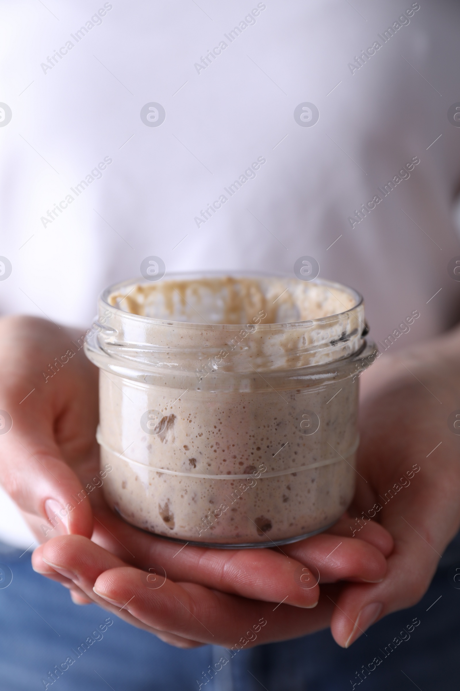 Photo of Woman holding glass jar with fresh sourdough starter, closeup