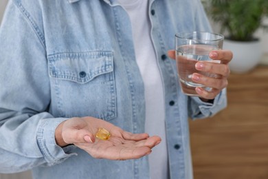 Photo of Woman with vitamin pills and glass of water indoors, closeup