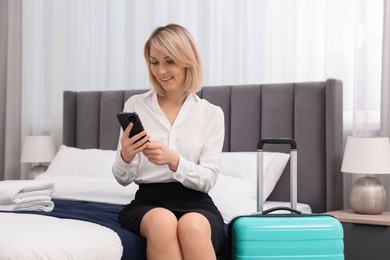 Photo of Smiling businesswoman with smartphone on bed in stylish hotel room
