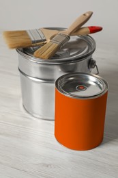 Can of orange paint, bucket and brushes on white wooden table