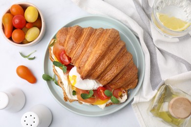 Tasty croissant with fried egg, tomato and microgreens served on white table, flat lay