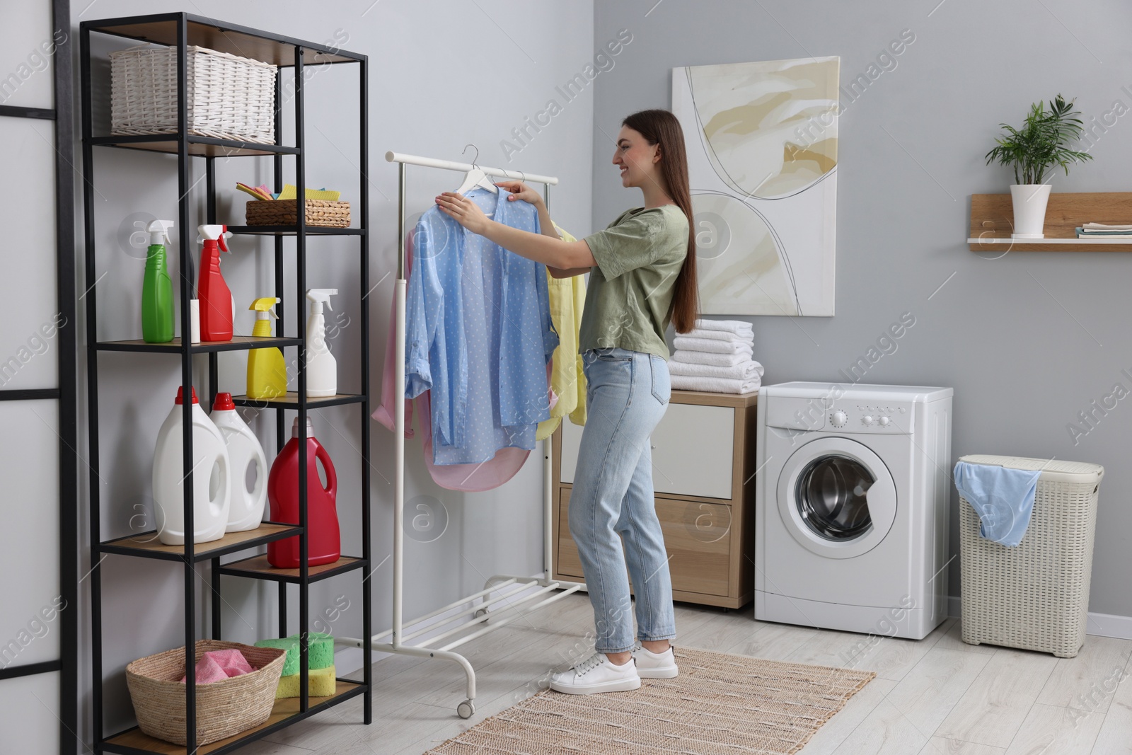 Photo of Young woman taking shirt from rack in laundry room