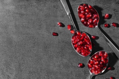 Spoons with pomegranate seeds on grey background, flat lay. Space for text