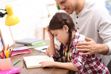 Photo of Man helping his daughter with homework at table indoors