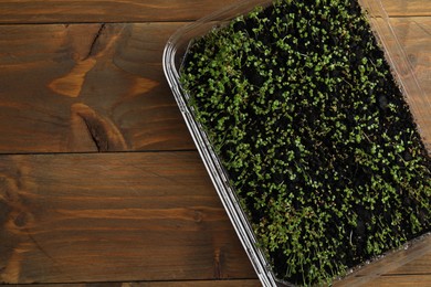Photo of Young arugula sprouts in container on wooden table, top view. Space for text