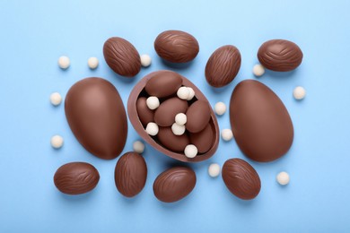 Photo of Delicious chocolate eggs and candies on light blue background, flat lay