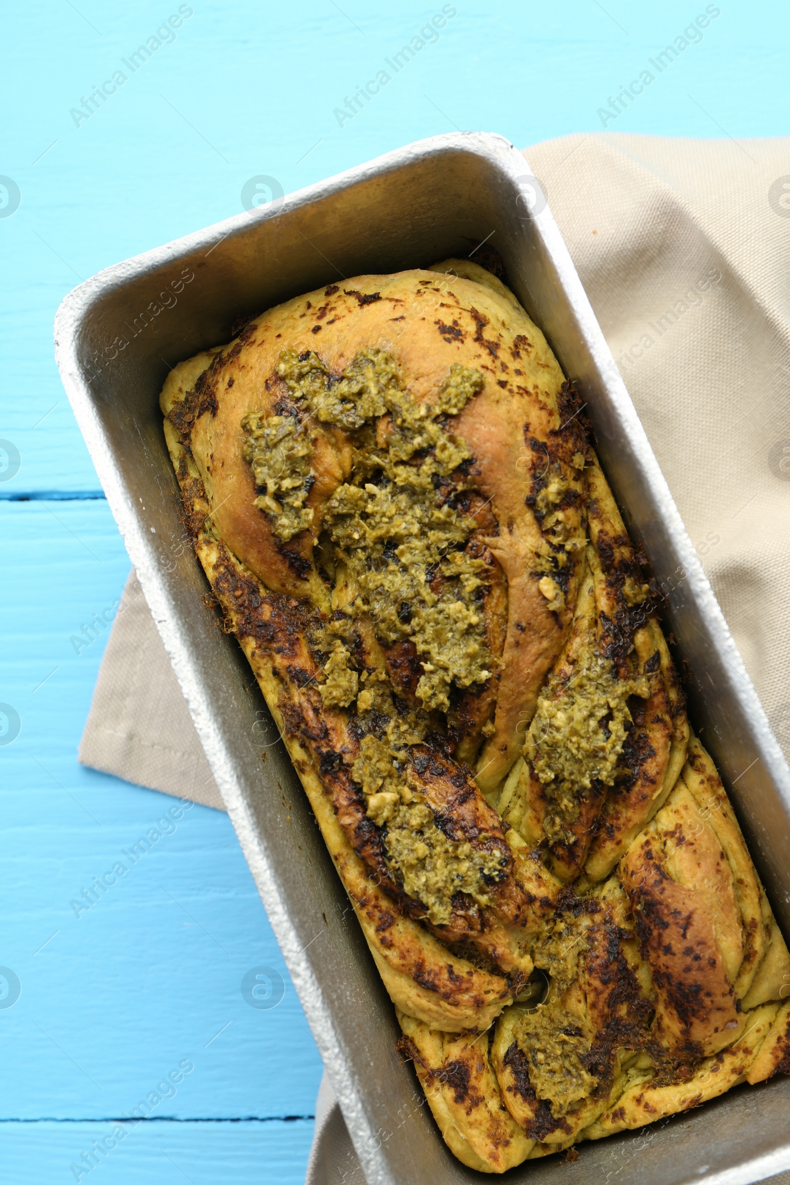 Photo of Freshly baked pesto bread in loaf pan on light blue wooden table, top view